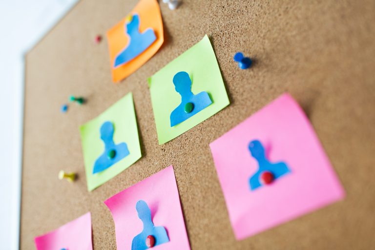 Paper people and notes on a cork board representing customer personas